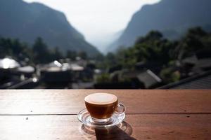 blick auf heiße milchtee latte art auf holztisch mit entspannender landschaft im dorf pha hee, chiang rai, thailand foto