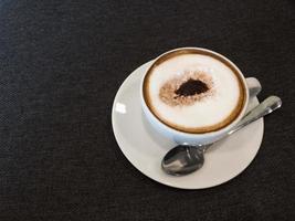 kaffee in weiß und stanless löffel auf schwarzem stoffhintergrund. kopierraum. foto