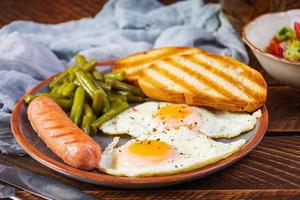 Frühstück mit Eiern, gegrillter Wurst, grünen Bohnen und Toast auf Holzhintergrund foto