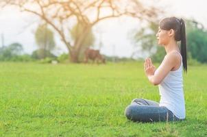junge Dame, die Yoga-Übungen im Außenbereich der grünen Wiese macht und Ruhe und Frieden im Meditationsgeist zeigt - Menschen praktizieren Yoga für Meditations- und Übungskonzept foto