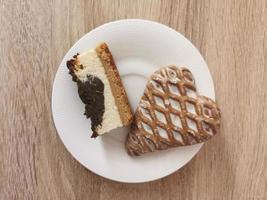 Ein Stück Käsekuchen und Lebkuchen in Herzform auf einem weißen Teller foto