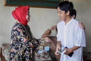 indonesische Volkstradition während der Eid Mubarak-Feier des Verteilens von Geld oder Thr genannt. großmutter gibt dem enkel der familie während idul fitri geld. foto