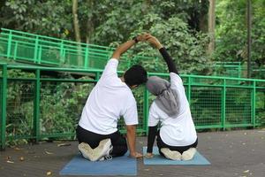 Rückansicht eines asiatischen muslimischen Paares, das Yoga auf einer Yogamatte im grünen Park macht. foto