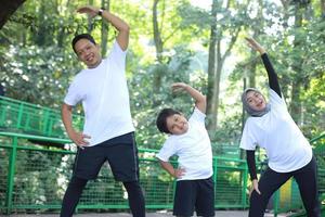 asiatische junge mutter und vater, die yoga praktizieren und sich zusammen mit ihrem sohn im grünen park dehnen. foto