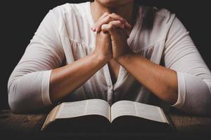 Nahaufnahme der Hand der christlichen Frau auf der Heiligen Bibel sind Gebet und Anbetung für Gott sei Dank in der Kirche mit schwarzem Hintergrund, Konzept für Glauben, Spiritualität und Religion foto