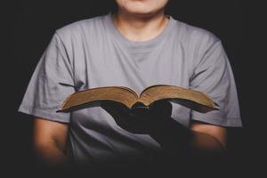 Nahaufnahme einer christlichen Frau, die die heilige Bibel hält, beten und anbeten, um Gott in der Kirche mit schwarzem Hintergrund zu danken, erwachsene weibliche Person liest Buch, foto