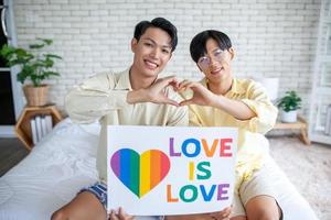 asiatisches homosexuelles paar, das zu hause ein lgbt-regenbogenschild hält, lgbtq-konzept. foto