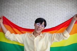 asiatischer schwuler, der zu hause lgbt-regenbogenfahne hält, lgbtq-konzept. foto