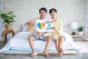 asiatisches homosexuelles paar, das zu hause ein lgbt-regenbogenschild hält, lgbtq-konzept. foto