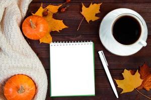 Herbstmorgenkonzept. tasse heißen espressokaffee und abgefallene blätter auf hölzernem hintergrund. Mockup-Notizbuch, Strickpullover und Kürbisse. foto