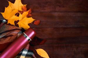 Herbst flach liegen. Thermoskanne mit heißem Kaffee, Plaid und abgefallenen Blättern auf Holzhintergrund. Beginn der Herbstsaison. foto