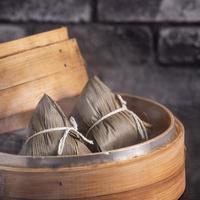 Reisknödel, Zongzi - chinesischer Reisknödel Zongzi auf schwarzem Backsteinhintergrund, Schiefertisch, Konzept des traditionellen Essens des Drachenbootfestivals, Nahaufnahme. foto