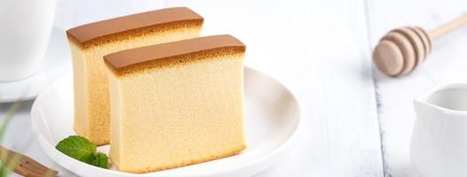 castella kasutera - schöne köstliche japanische geschnittene schwammkuchennahrung auf weißer platte über rustikalem weißem holztisch, nahaufnahme, kopierraum-designkonzept. foto