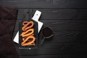 hausgemachte Churros mit Schokolade auf dunklem Holz rustikalen Hintergrund. foto