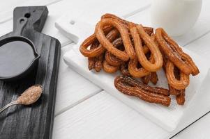 hausgemachte Churros mit Schokolade auf weißem Holzhintergrund. foto