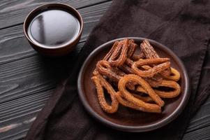 hausgemachte Churros mit Schokolade auf dunklem Holz rustikalen Hintergrund. foto