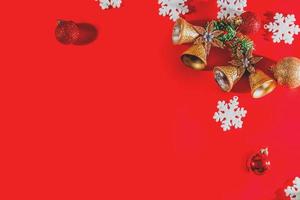 Weihnachtshintergrundkonzept. Draufsicht der goldenen Weihnachtsglocken mit Kugeldekoration, Fichtenzweigen, Stern und Schneeflocken auf rotem Hintergrund. foto