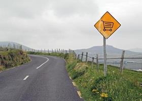 Gelbes Schild mit Einkaufswagen an einer kurvenreichen Straße foto