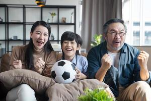asiatische familie, die fußballsportspiele im fernsehen sieht und glücklich reagiert, wenn das team den ball ins tor schießt. foto