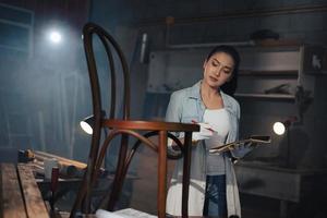 junge asiatische Designermöbel Frau Zimmermann misst mit einem Maßband den Stuhl auf der Werkbank in der Holzwerkstatt. foto