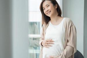 Porträt eines jungen asiatischen schwangeren Mädchens, das zu Hause nach draußen schaut foto