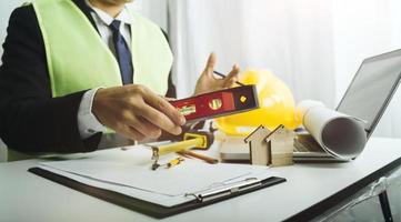 Zwei Kollegen diskutieren über Datenverarbeitung und Tablet, Laptop mit einem Architekturprojekt auf der Baustelle am Schreibtisch im Büro foto