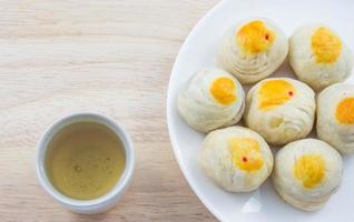 Chinesisches Gebäck Mungobohnen oder Mondkuchen mit Eigelb auf Teller Holztisch und grüner Teetasse foto