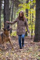 junge süße frau, die draußen im herbstwald mit deutschem schäferhund spielt foto