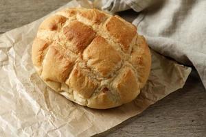 hausgemachtes Boule-Rundbrot auf braunem Papier, rustikaler Holztisch. foto