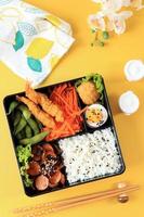 apanesische Bento-Lunchbox mit gedämpftem Gemüse, gekochtem Ei, Nugget, Wurst, Edamame und Tempura foto