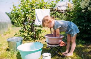 Kleines Vorschulmädchen hilft beim Waschen. Kind wäscht Kleidung im Garten foto