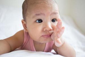 asiatisches süßes baby im weißen sonnigen schlafzimmer. neugeborenes kind entspannt sich im bett foto