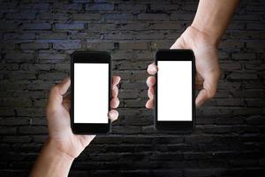 Zwei Hände halten den leeren Bildschirm eines Smartphones an der alten schwarzen Ziegelwand. foto