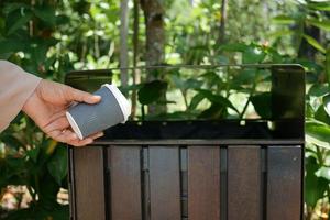 Frauen werfen eine leere Kaffeetasse aus Papier in den Mülleimer oder Mülleimer foto