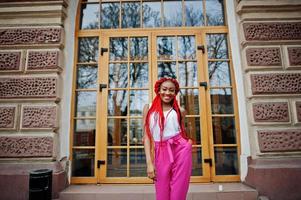 Modisches afroamerikanisches Mädchen in rosa Hosen und roten Dreads posierte im Freien. foto