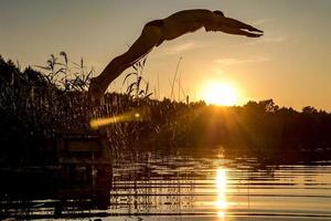 Mann taucht bei Sonnenuntergang in das Wasser des Sees foto