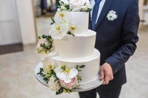 Der Bräutigam trägt eine festliche, mit weißen Rosen geschmückte Hochzeitstorte foto