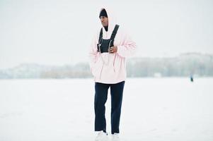 stilvoller afroamerikanischer mann im urbanen stil in rosa kapuzenpulli posierte im winter am zugefrorenen see. foto