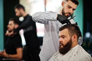 hübscher bärtiger mann im friseursalon, friseur bei der arbeit. foto