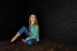 stylisches blondes Mädchen in Jacke und Jeans gegen schwarze Ziegelwand im Studio. foto