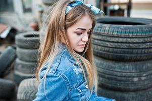 Junges Hipster-Mädchen in Jeansjacke und Kopftuch in der Reifenmontagezone. foto