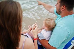 Sommerferien. eltern und menschen outdoor-aktivitäten mit kindern. schöne Familienferien. vater, schwangere mutter, kleine tochter, die auf sonnenliege am seesandstrand sitzt. foto