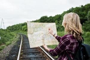 Porträt eines hübschen blonden Mädchens im Tartanhemd, das mit einer Karte in den Händen auf der Eisenbahn spazieren geht. foto