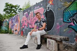 Lifestyle-Porträt eines gutaussehenden Mannes, der auf der Straße der Stadt mit Graffiti-Wand posiert. foto