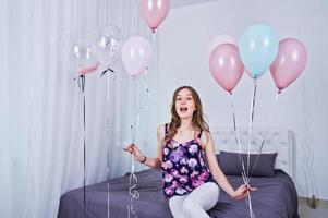 glückliches Mädchen mit farbigen Luftballons auf dem Bett im Zimmer. Geburtstagsthema feiern. foto