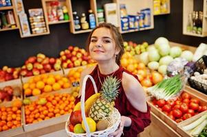 Mädchen in Rot, das verschiedene Früchte und Gemüse im Korb im Obstladen hält. foto