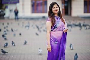 Indisches hinduistisches Mädchen im traditionellen violetten Saree posierte auf der Straße gegen Tauben. foto