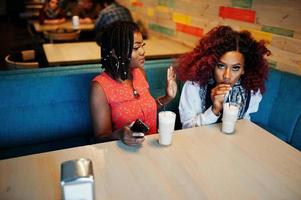 Attraktive afroamerikanische zwei Freundinnen sitzen im Café mit Latte. foto