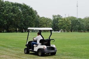 mann, der golfauto auf dem golfplatz fährt. foto