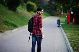 junger indischer studentenmann in rot kariertem hemd und jeans mit rucksack posierte auf der straße. foto